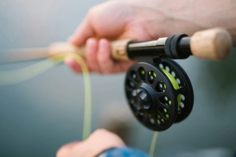 A close up picture of someone holding a fishing pole with green line coming out of the spool.