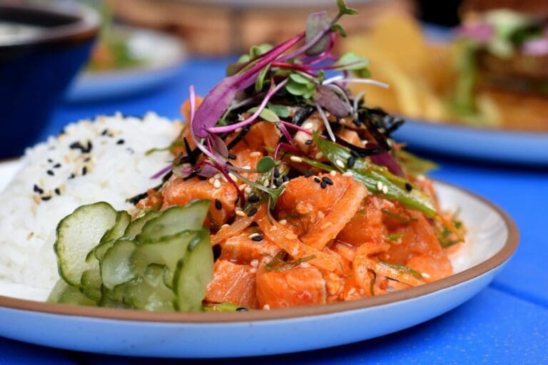 A plate with fish, cucumbers, rice and greens.