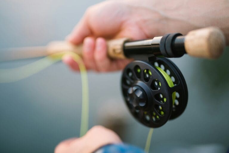 A close up picture of someone holding a fishing pole with green line coming out of the spool.