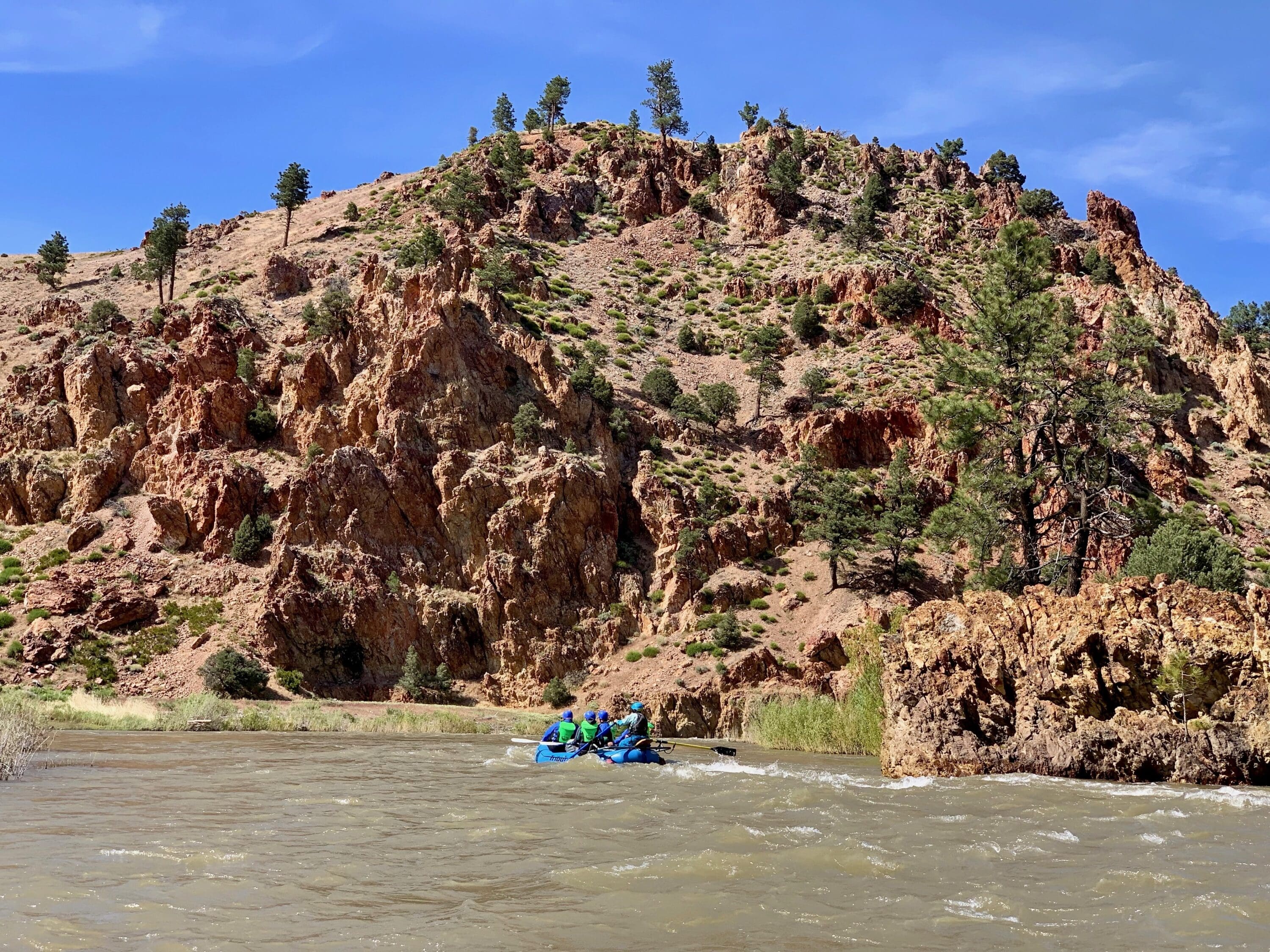A rafting boat floating down the Carson River with red rocks behind it.