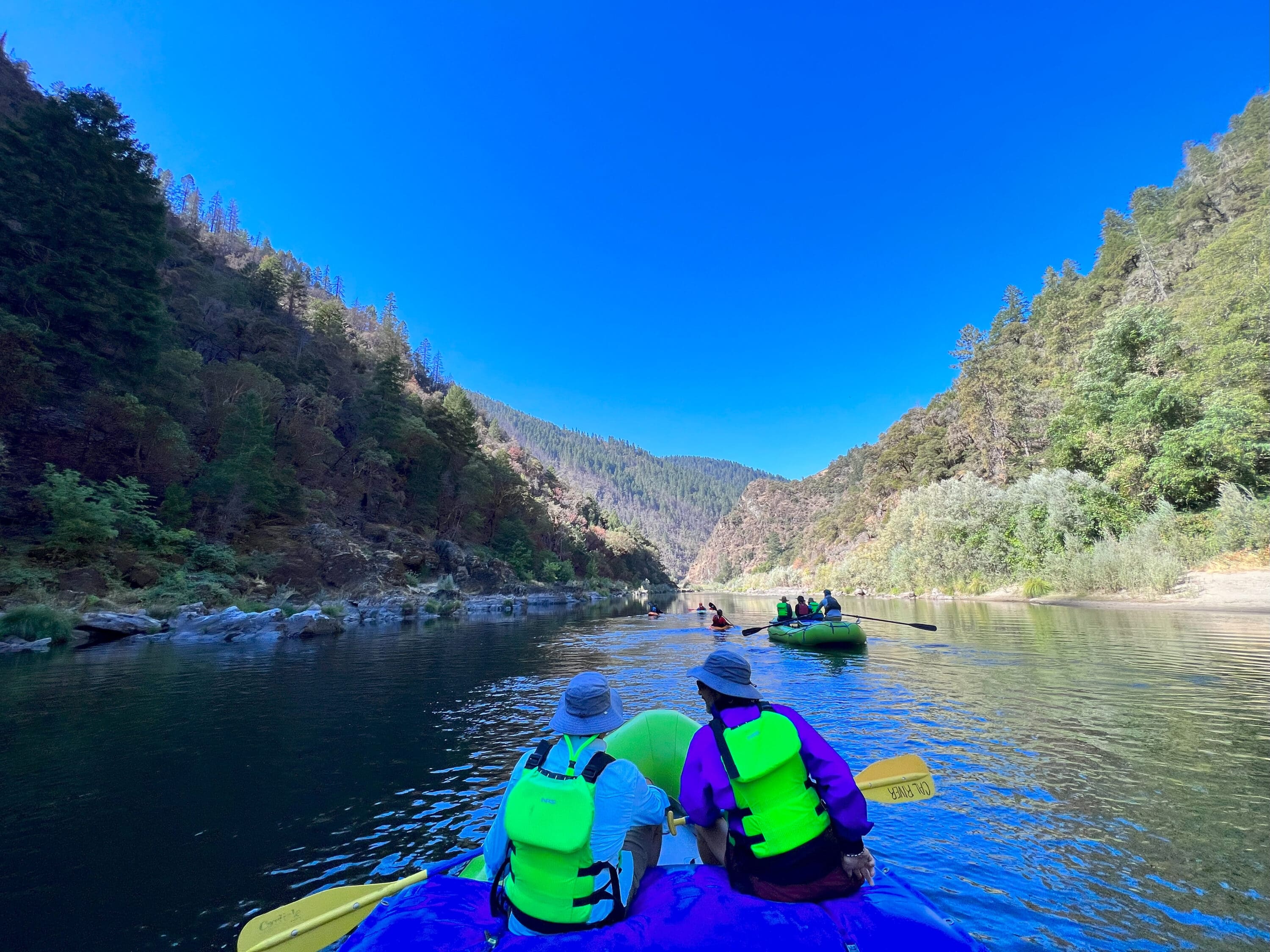 People in rafting boats padding down the rogue river in a beautiful canyon.