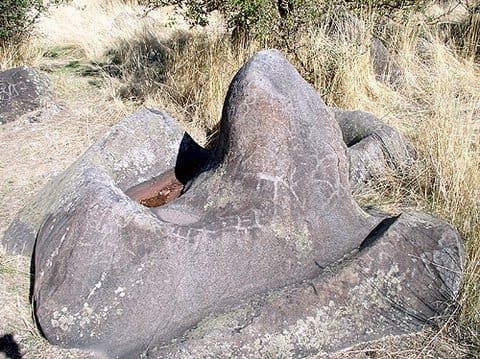 Red rock formation surrounded by dry grass.