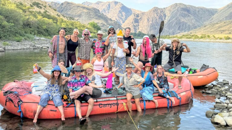 Large ground of people on and around an orange rafting boat. Everyone is having fun, dressed in costumes holding paddles.