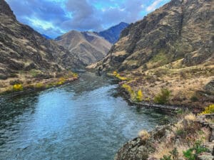 River running through a deep canyon with mountains on both sides. River is lines with colorful trees while the mountains are mostly rock and brush.